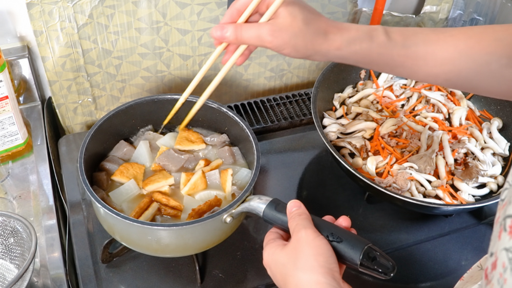鍋で煮物を作りながら隣のフライパンで野菜ときのこを調理する様子